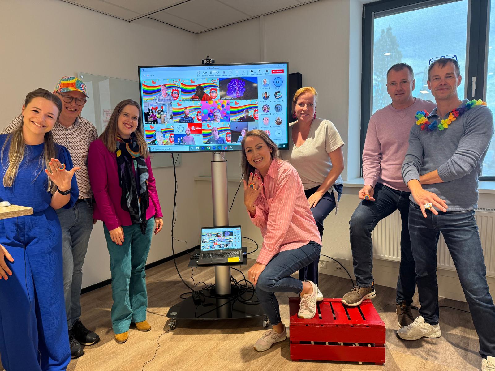Group of people in a room with a screen showing a video call.