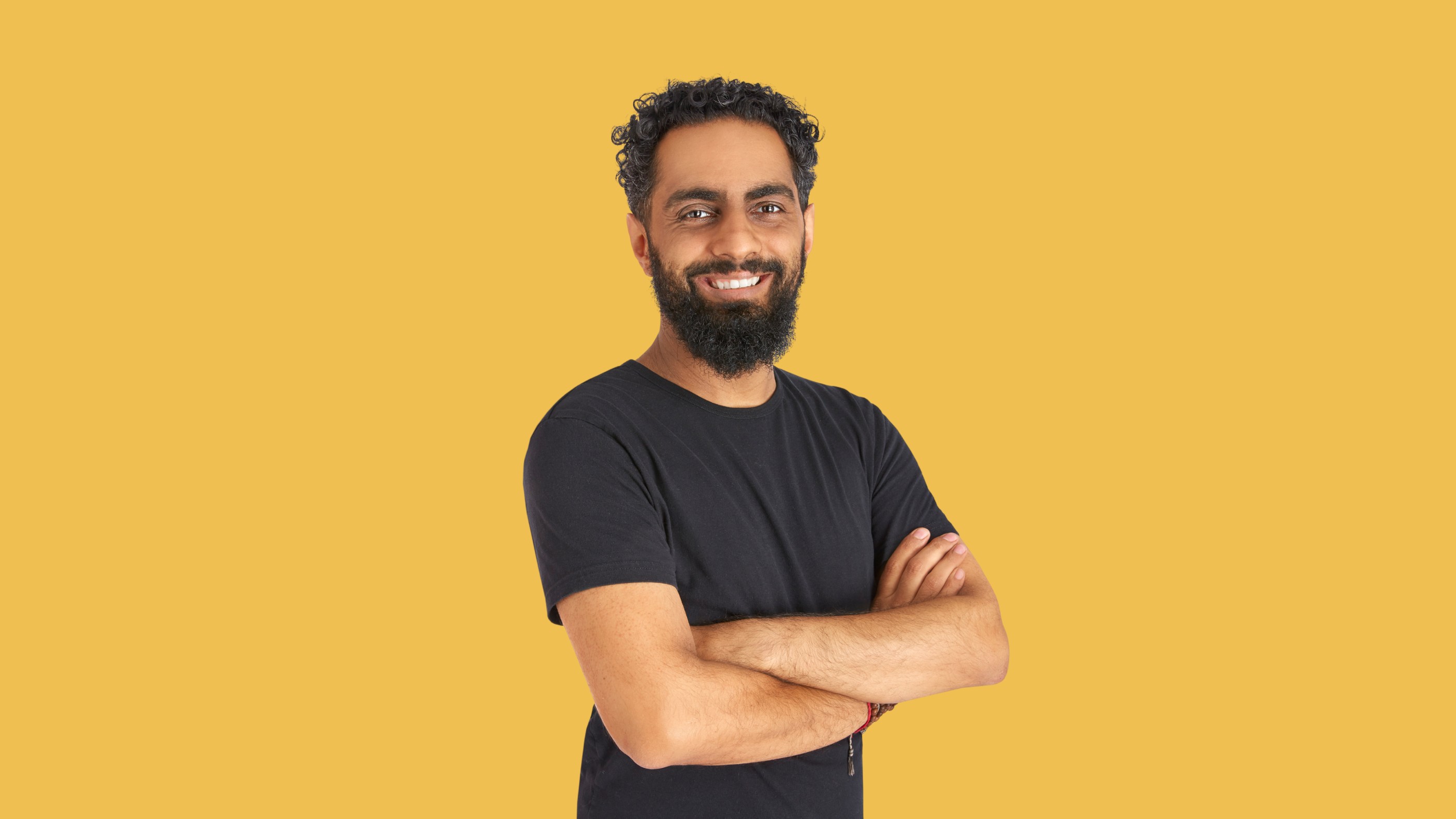 Man with beard, black shirt, arms crossed, yellow background.