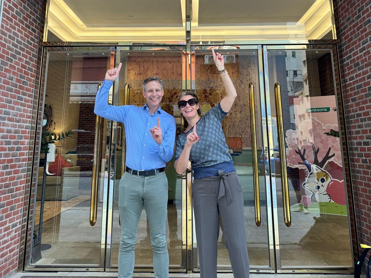 Two people pointing up in front of a building with glass doors.