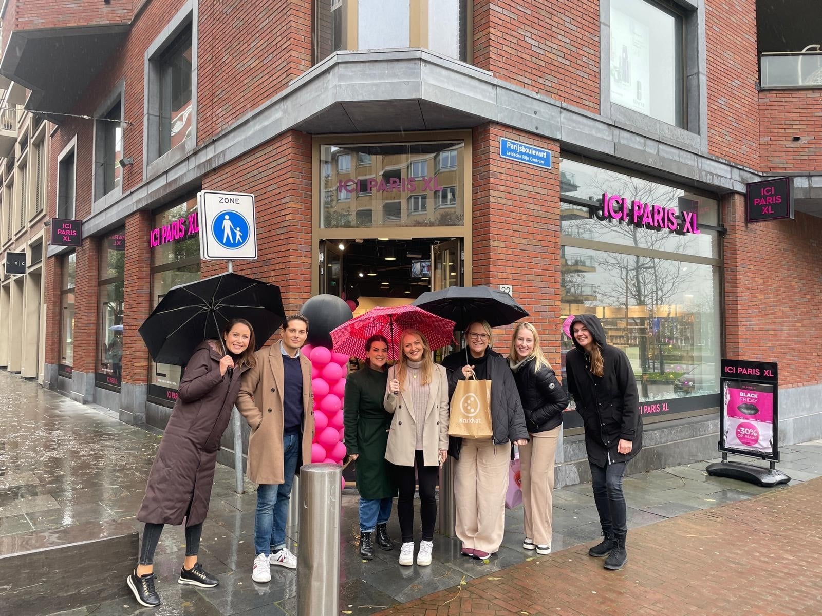 Group of people with umbrellas in front of a store.