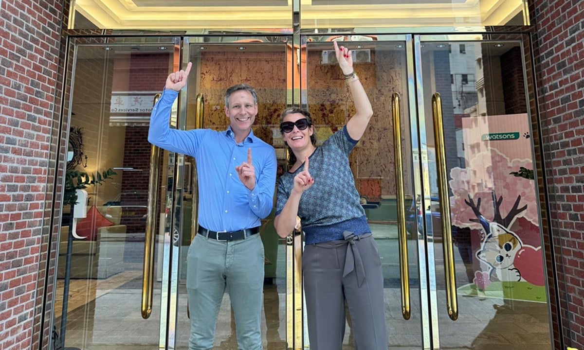 Two people pointing up in front of a building with glass doors.