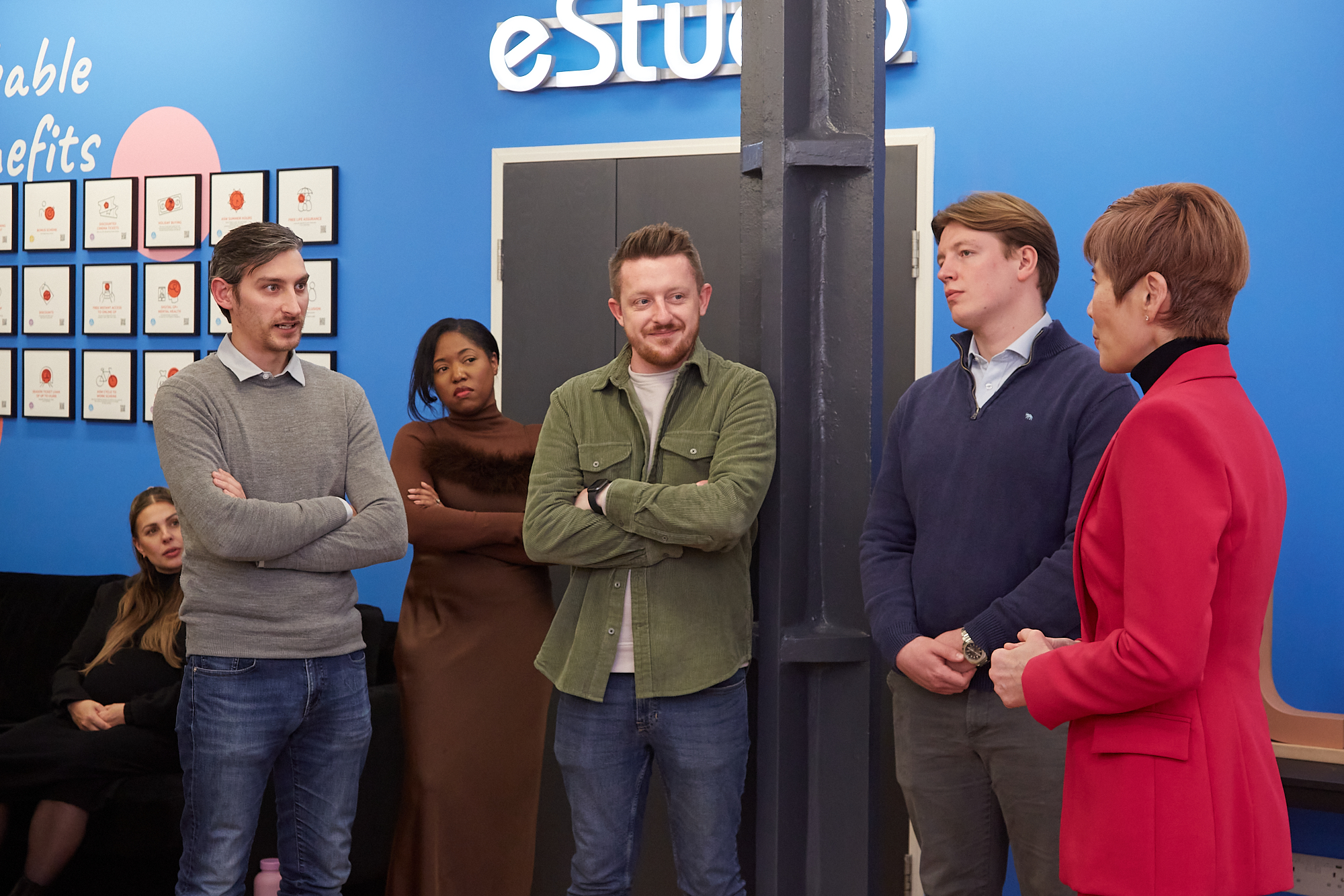 Group of people in a meeting, blue wall background.