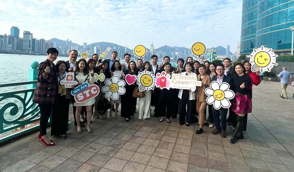 Group of people holding signs, smiling, posing for a photo. Cityscape in the background.