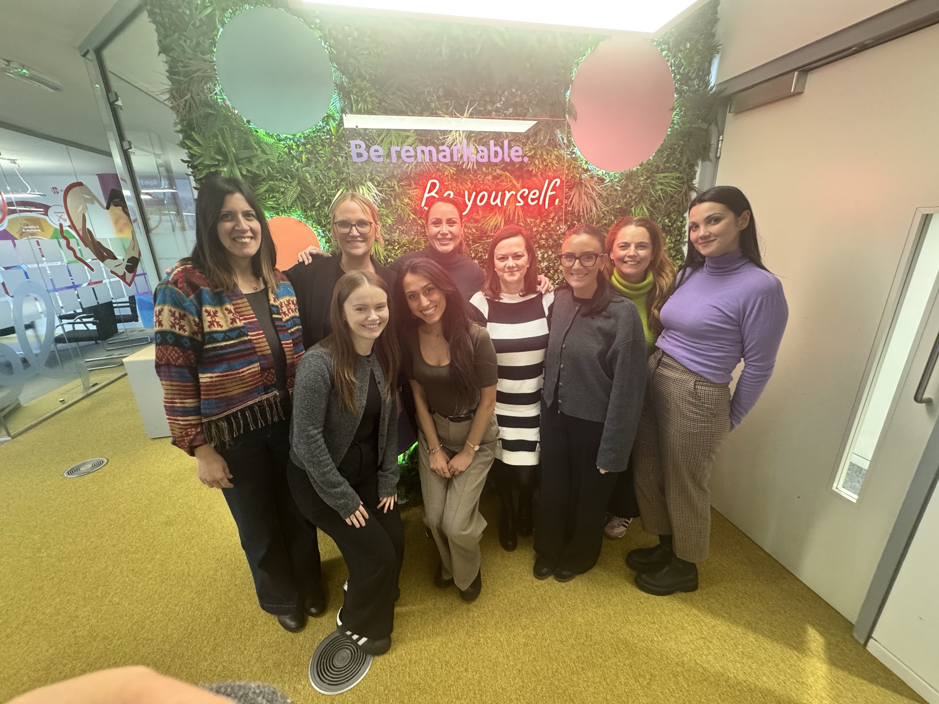 Group of women posing for a photo in front of a wall with neon sign.