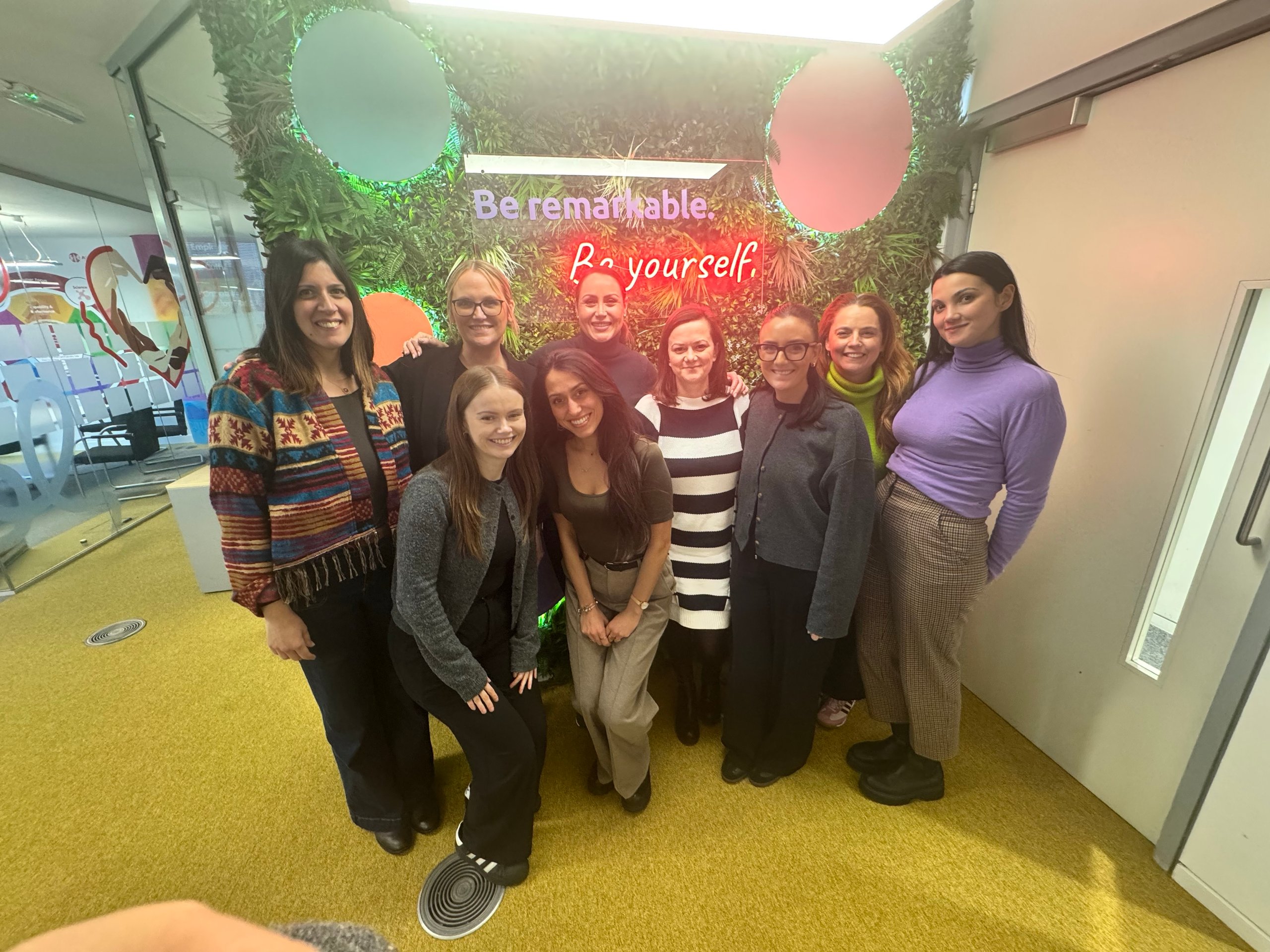 Group of women posing for a photo in front of a wall with neon sign.