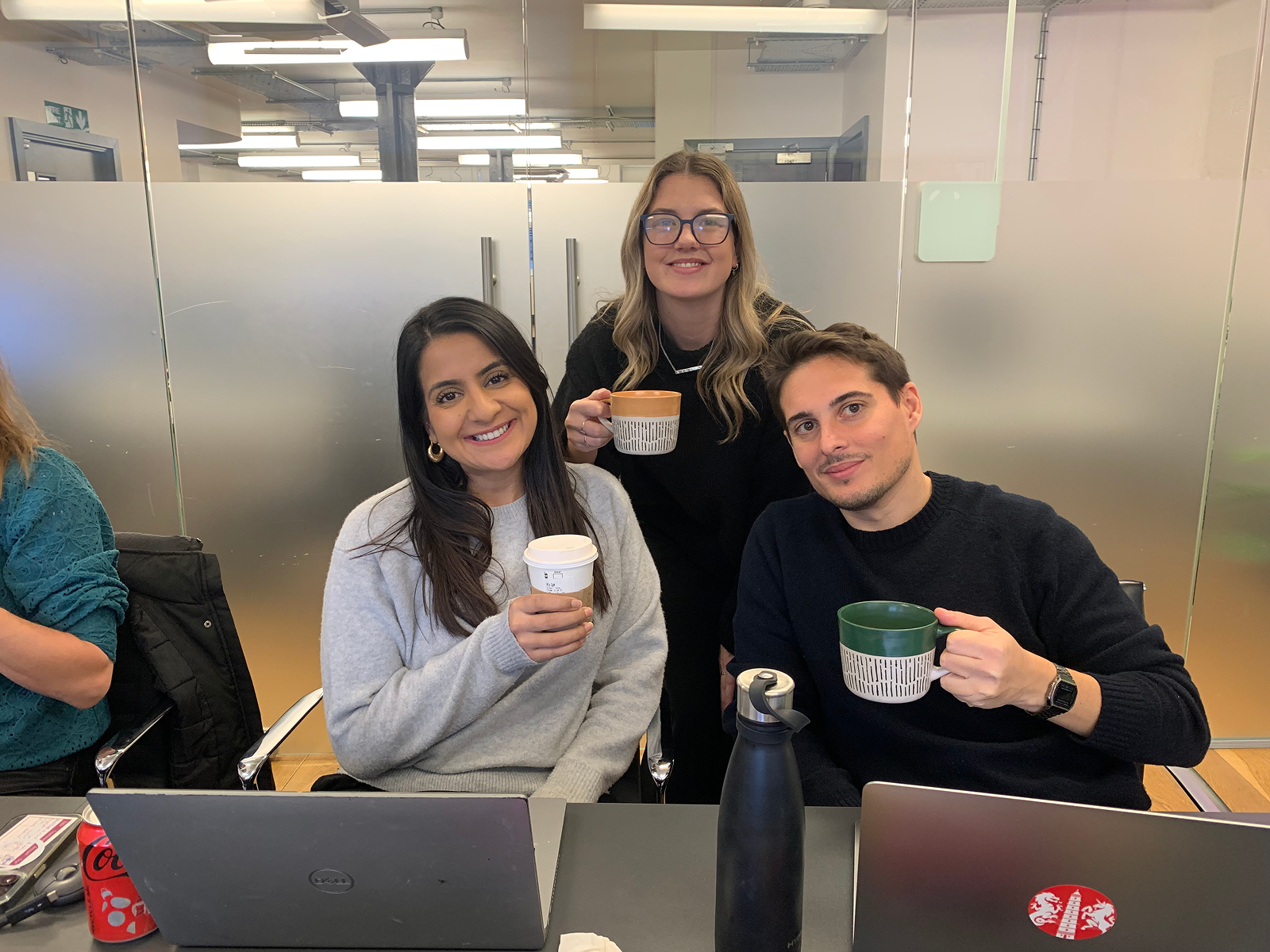 Three people holding coffee cups, smiling at the camera.