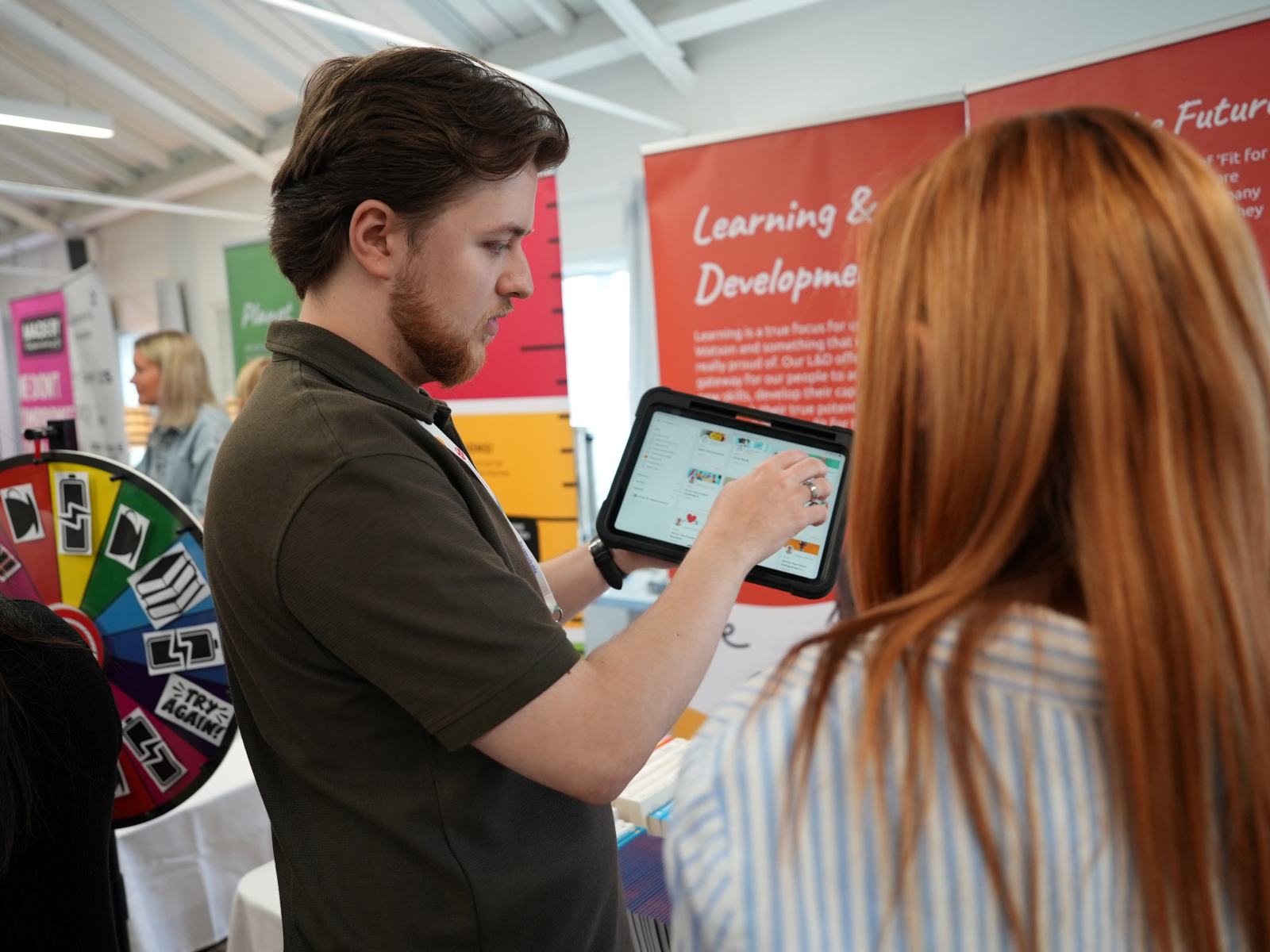 Man showing tablet to woman, event with learning and development theme.