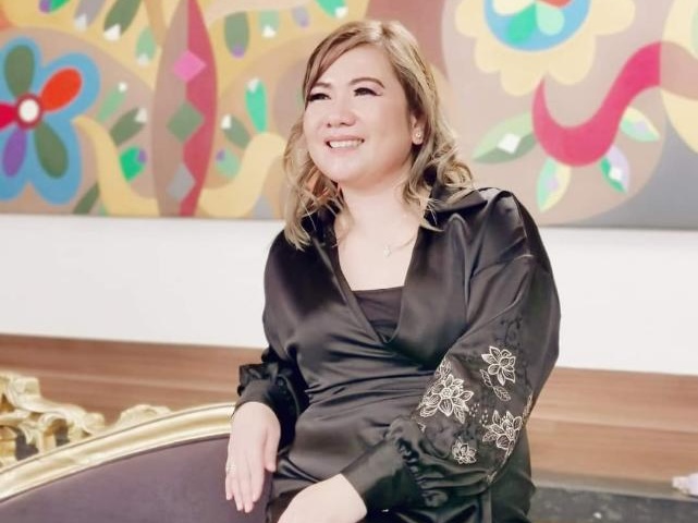 Woman smiling, wearing a black dress with floral embroidery on the sleeves.
