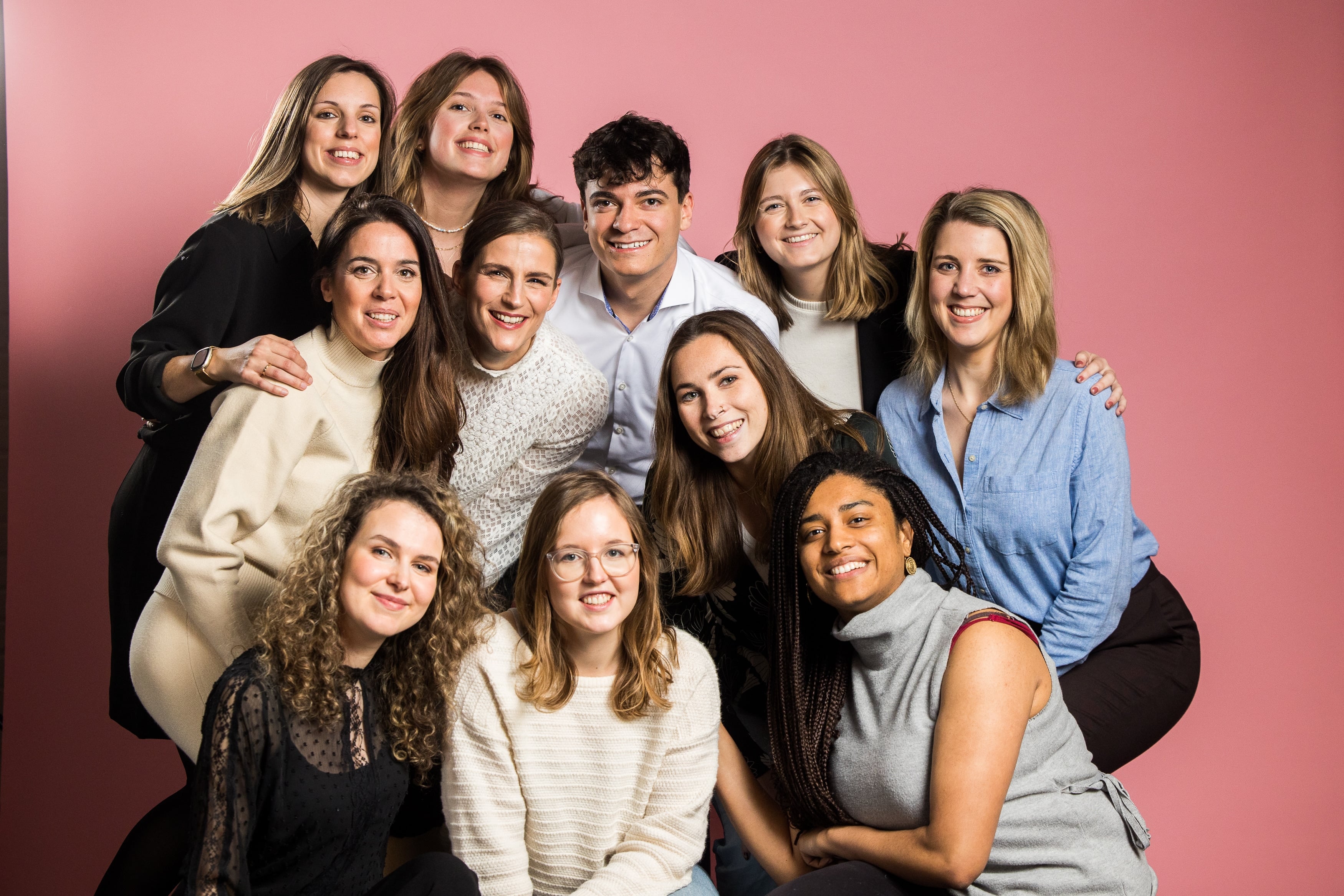 Group of smiling people posing together against a pink background.