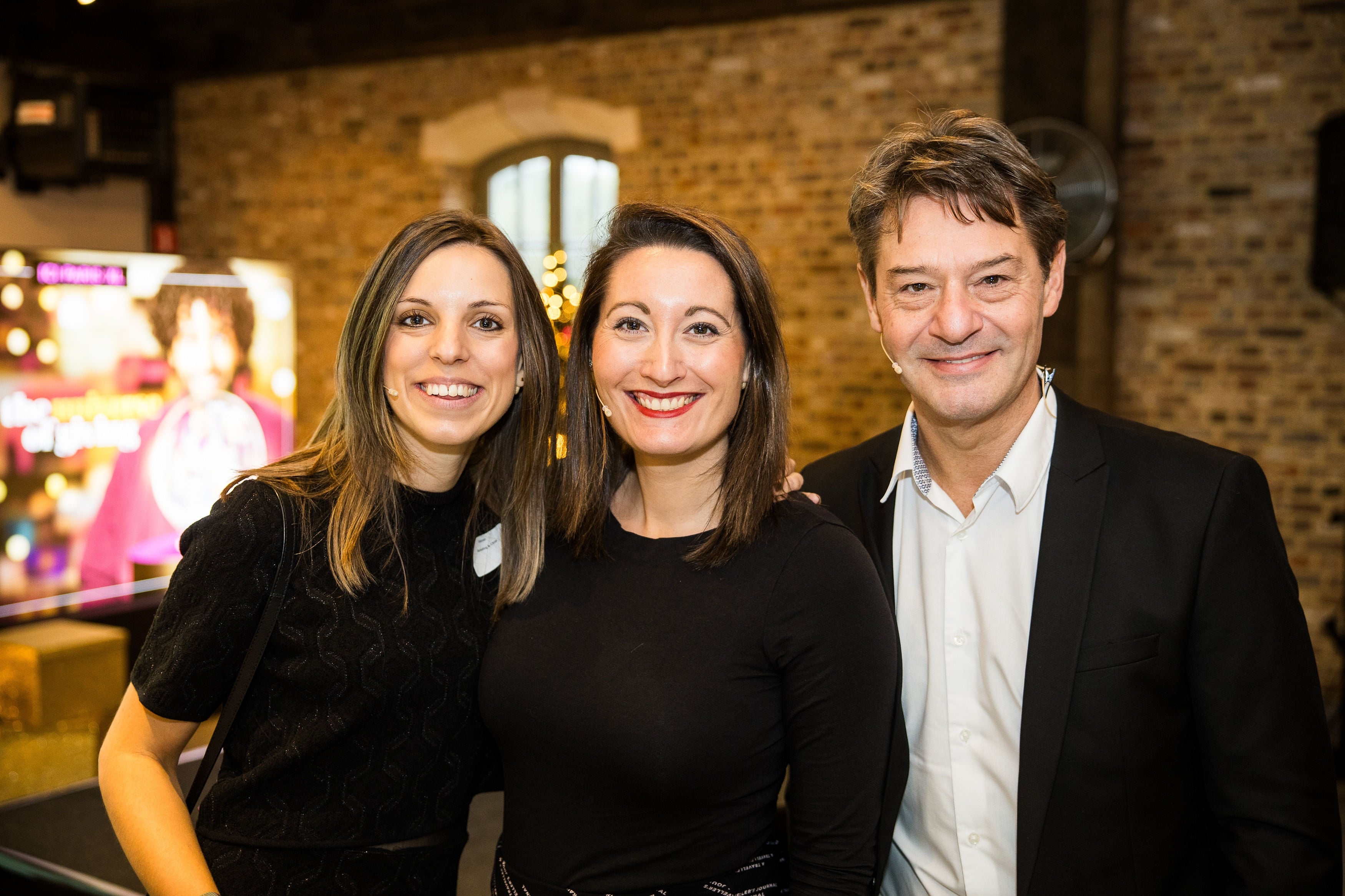 Three people smiling at the camera, brick wall background.