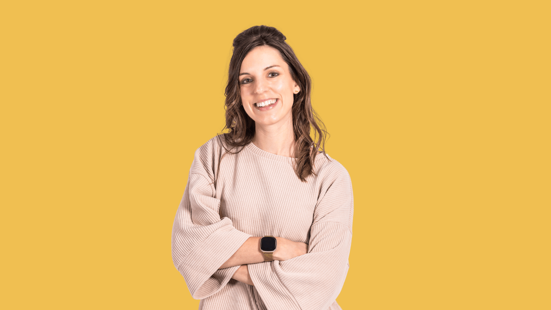 Woman smiling with arms crossed, wearing a watch, yellow background.