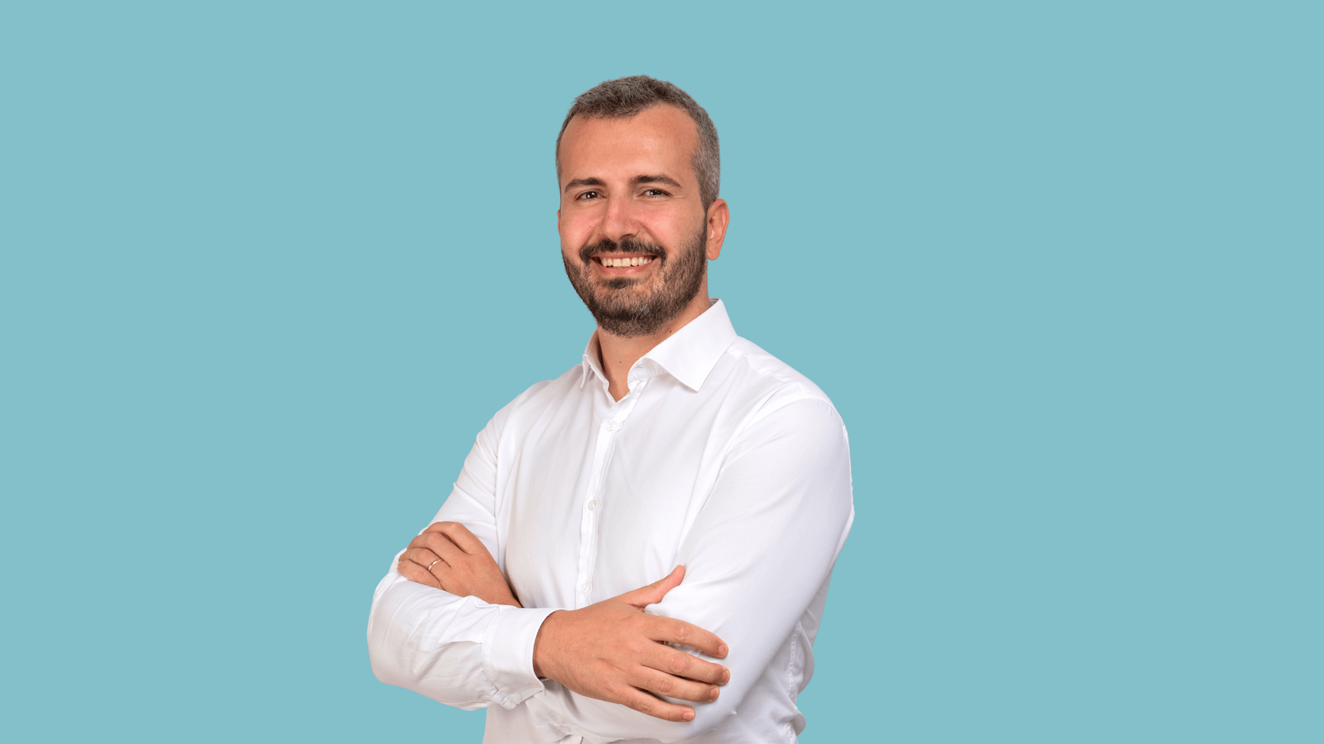 Man in white shirt smiling with arms crossed, blue background.