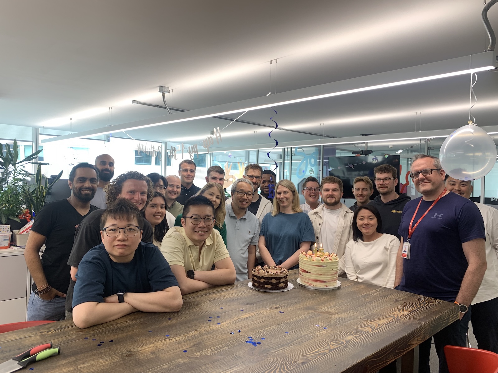 Group of people celebrating with cakes and balloons.