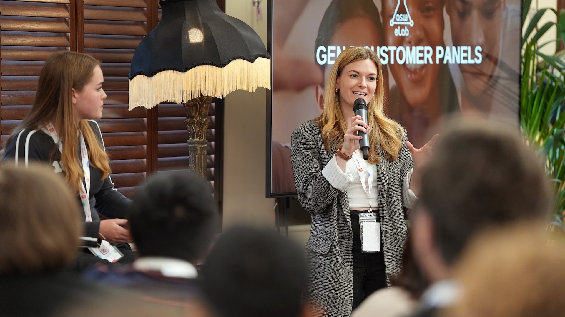Woman speaking into a microphone at a conference, with a screen in the background.