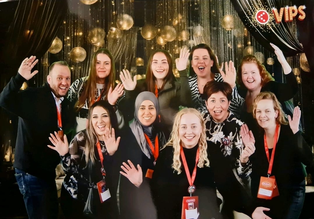 Group of people waving to the camera at an event with decorations.
