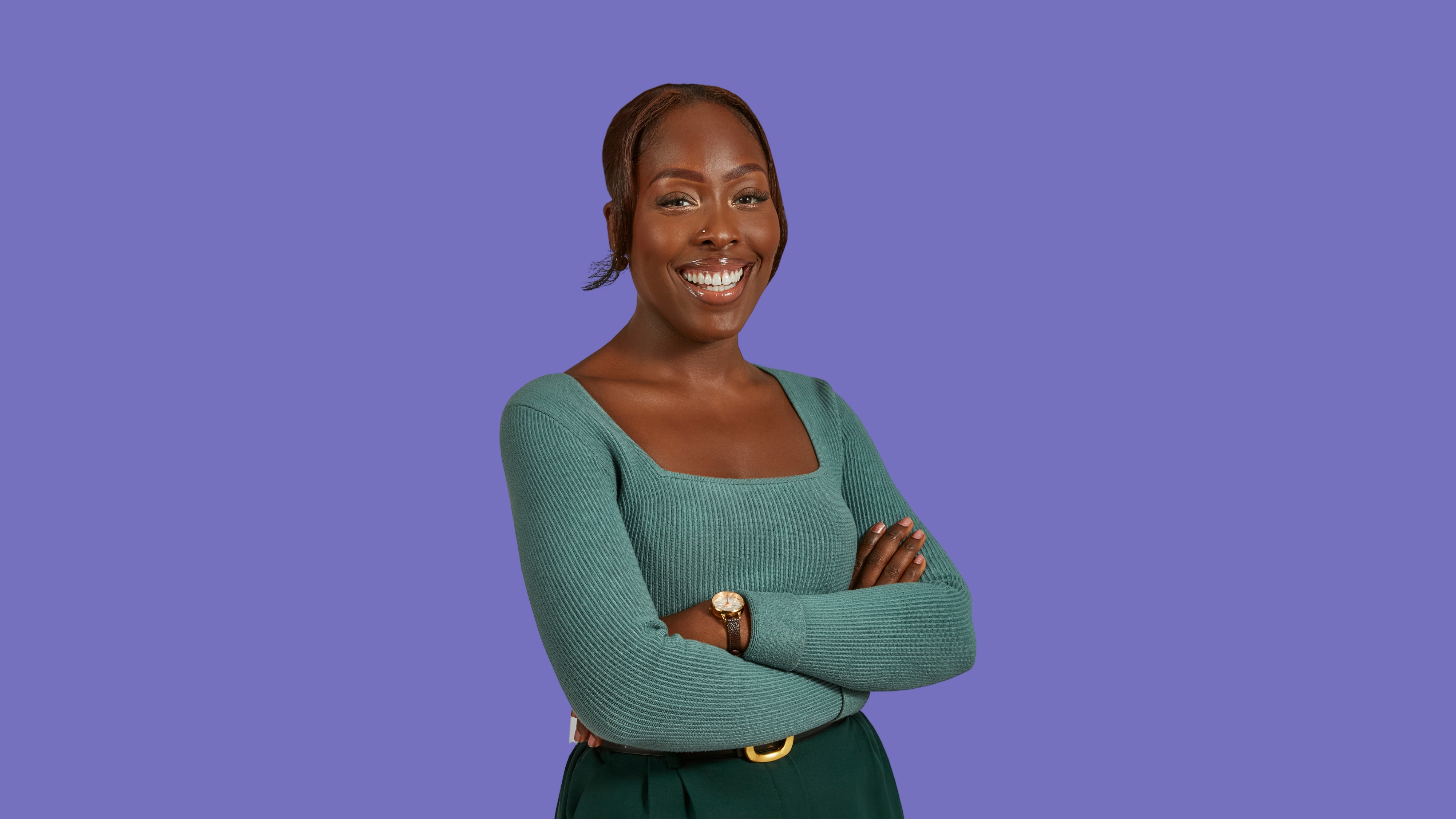 Woman smiling with arms crossed, teal top and purple background.